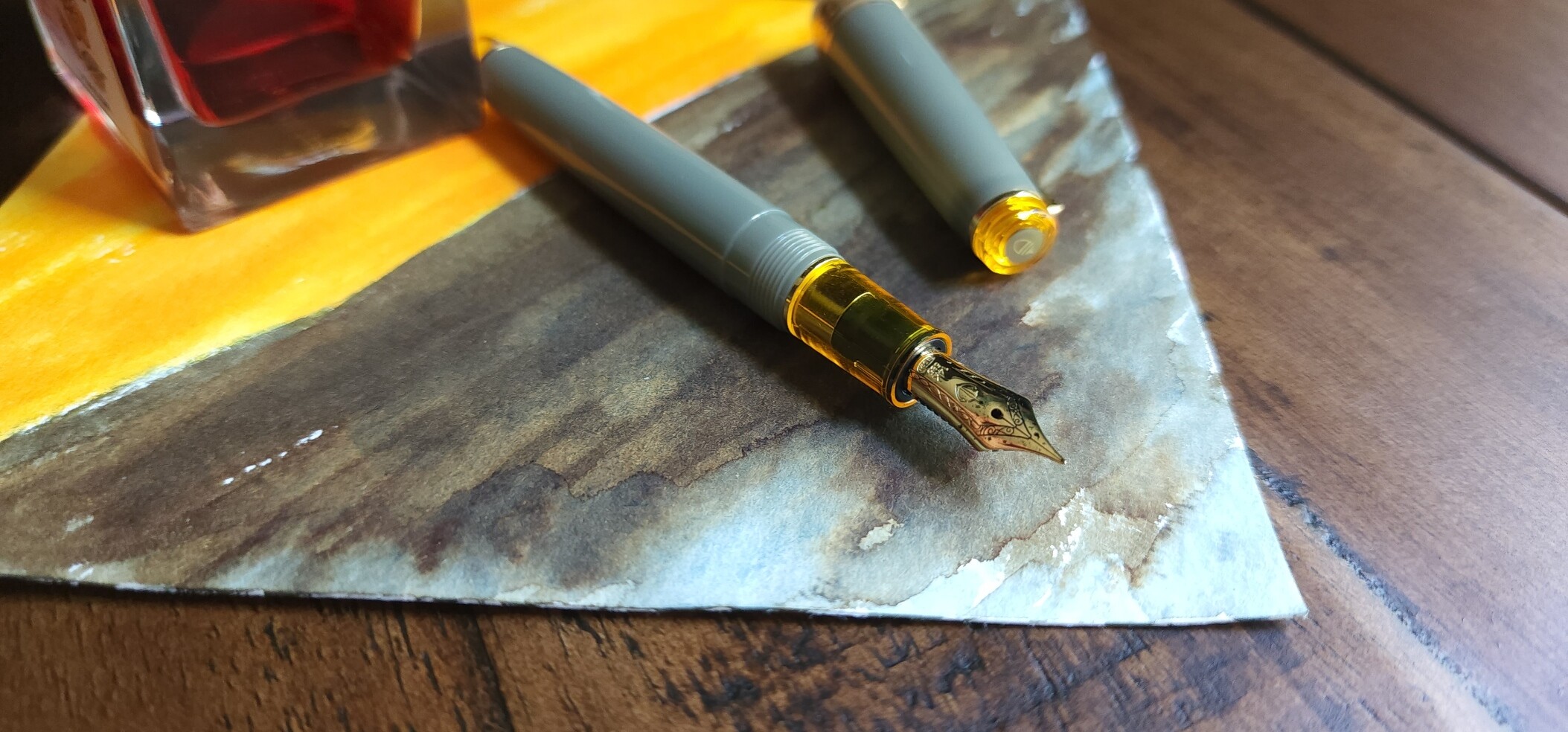 Sailor Pro Gear Slim 'Nuts' pen with a medium gold nib and light gray green translucent body with transparent yellow accents with swatches of the green/brown/blue Sailor Manyo Shirakashi and bright yellow Sailor Manyo Yamabuki inks.