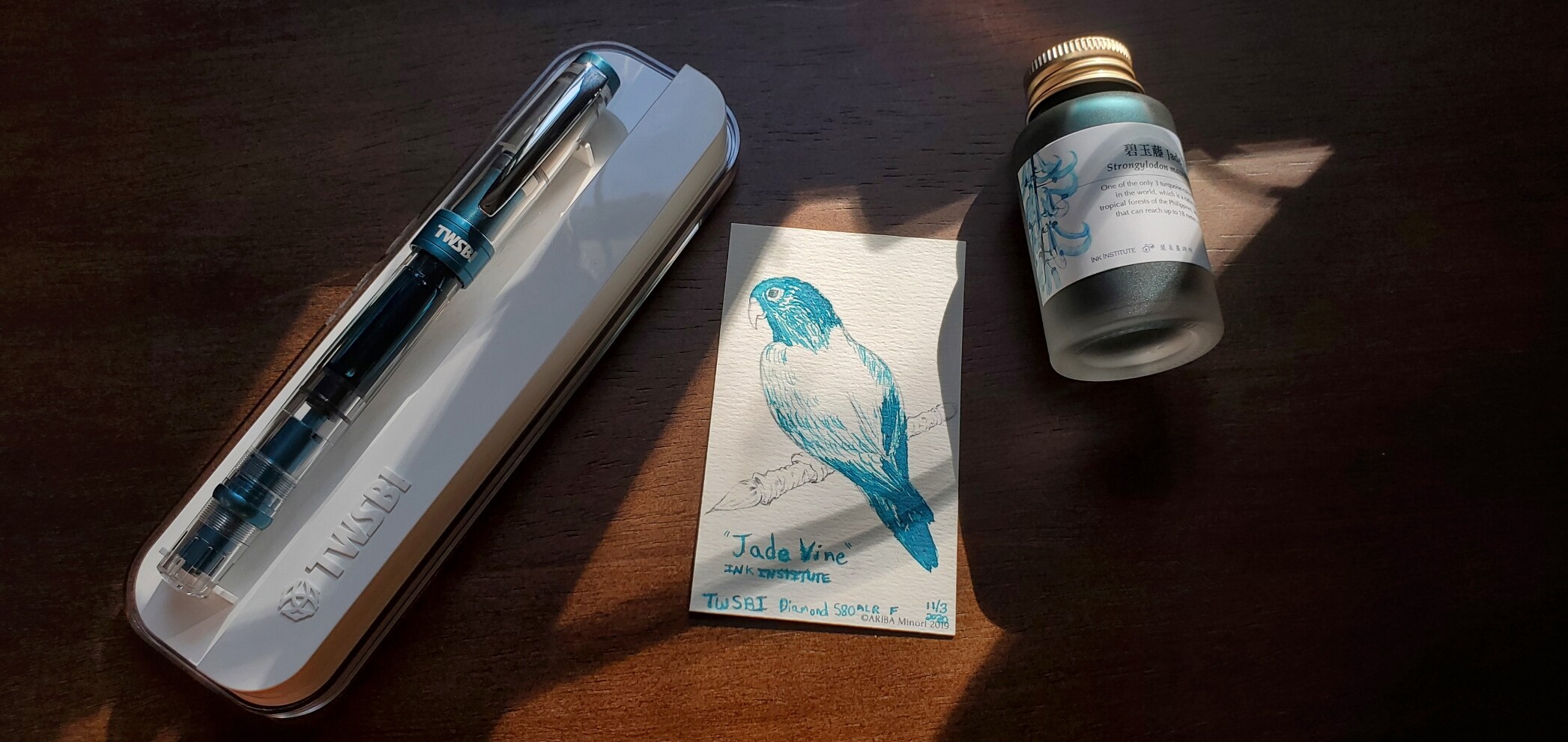 TWSBI Diamond 580 ALR in Prussian Blue with Ink Institute Jade Vine ink and a swatch card with a bird outline colored in and labeled with the Jade Vine ink.