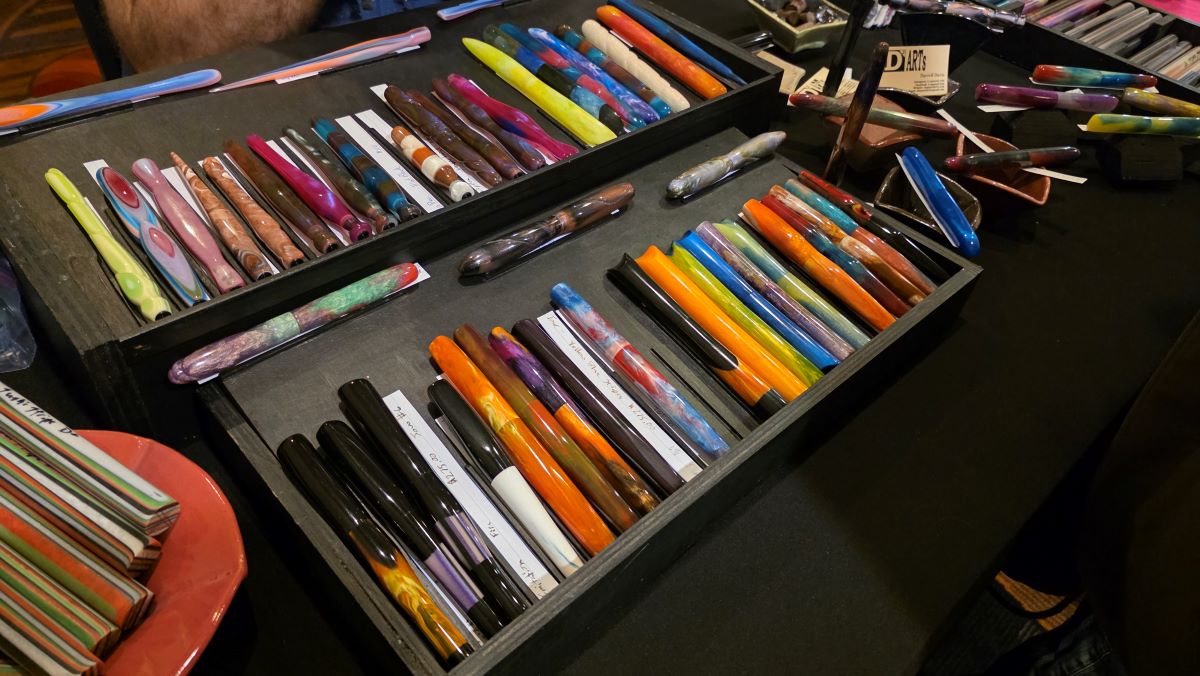 Two rows of unique, hand-carved fountain pens and dip nib holders available for sale.