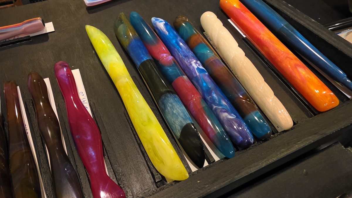 Closeup of several hand carved fountain pens and nib holders, including a bright yellow-green resin carved into the shape of a propeller blade.