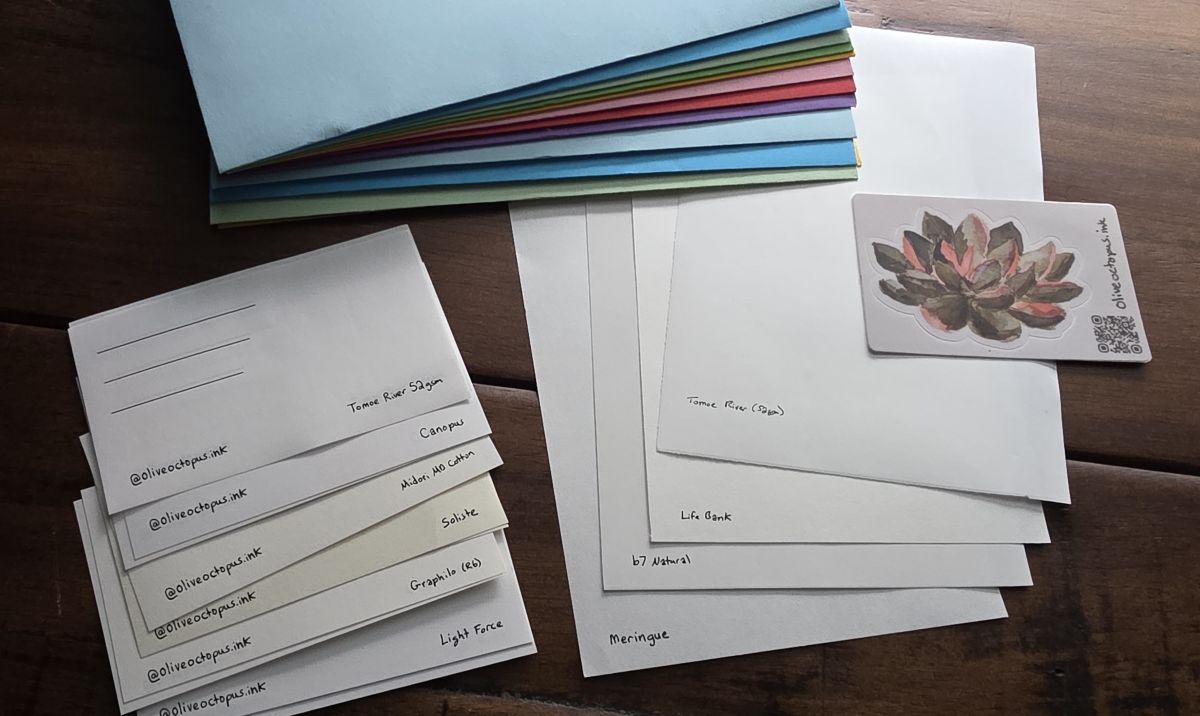 Stack of colored envelopes and several sheets and swatch cards of different fountain pen papers.