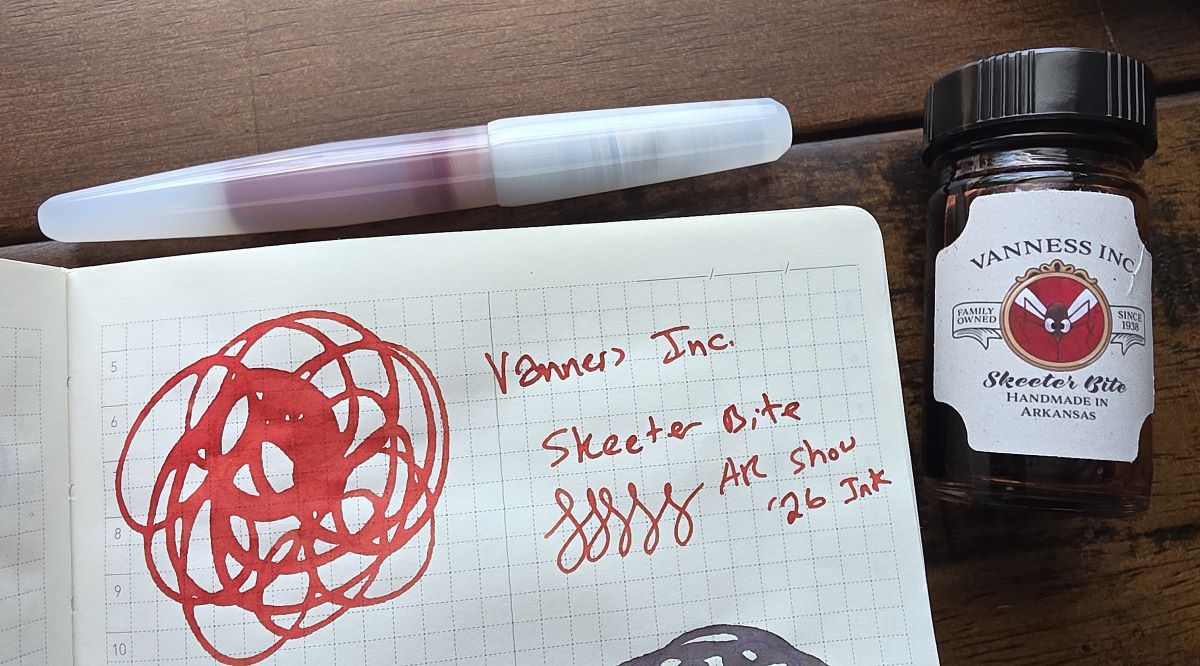 Bottle and writing sample of the light red Vanness Skeeter Bite fountain pen ink next to a translucent white fountain pen filled with the red ink.