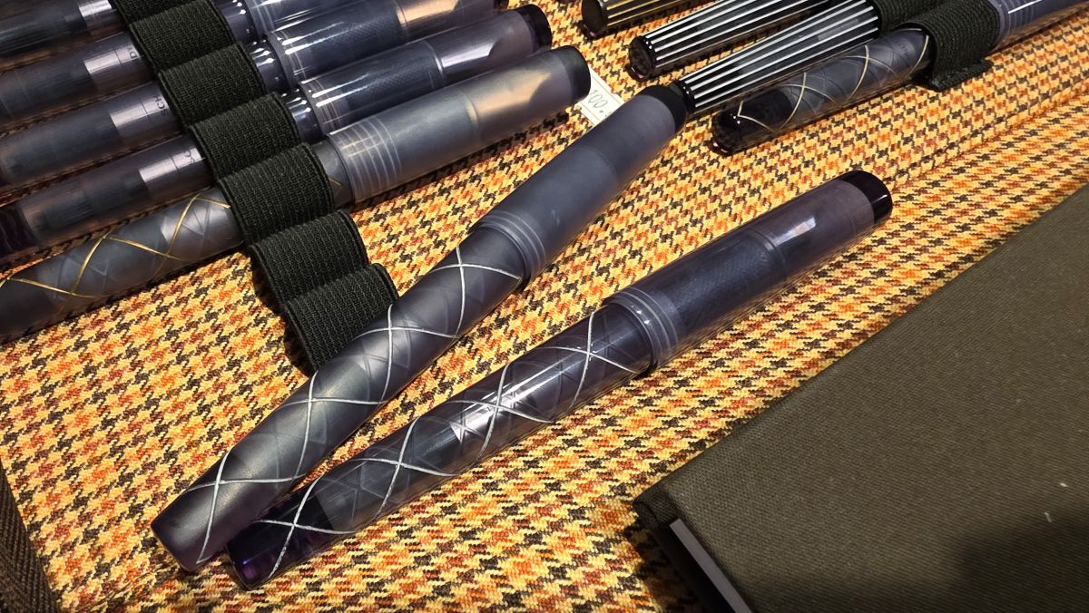 A binder of fountain pens in translucent gray material and some with different silver or gold designs and both polished and matte finishes.