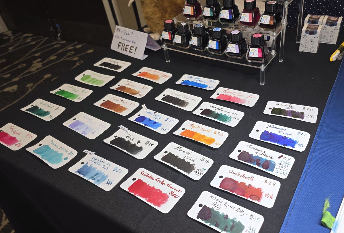 The Kiwi Inks table with several rows of ink swatches and bottles of fountain pen inks.