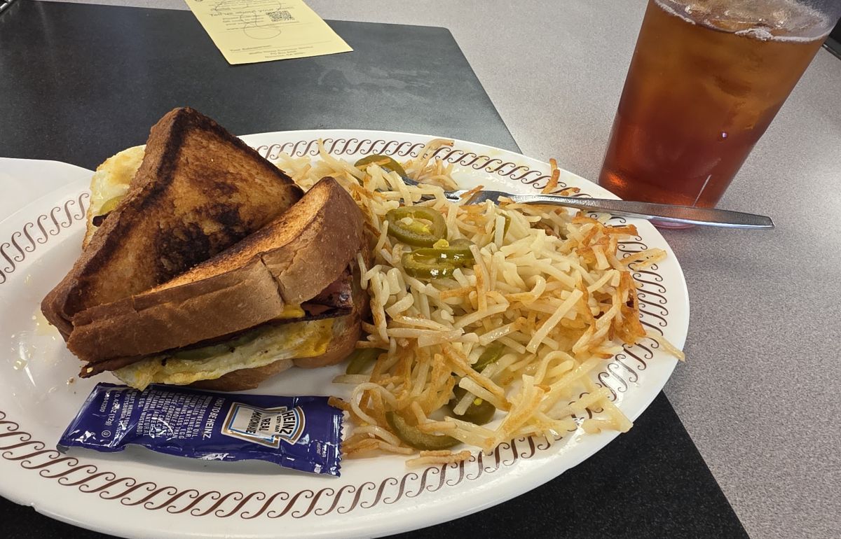 Breakfast at Waffle House including a breakfast sandwich on Texas toast, hashbrowns with jalapeños, and iced tea.