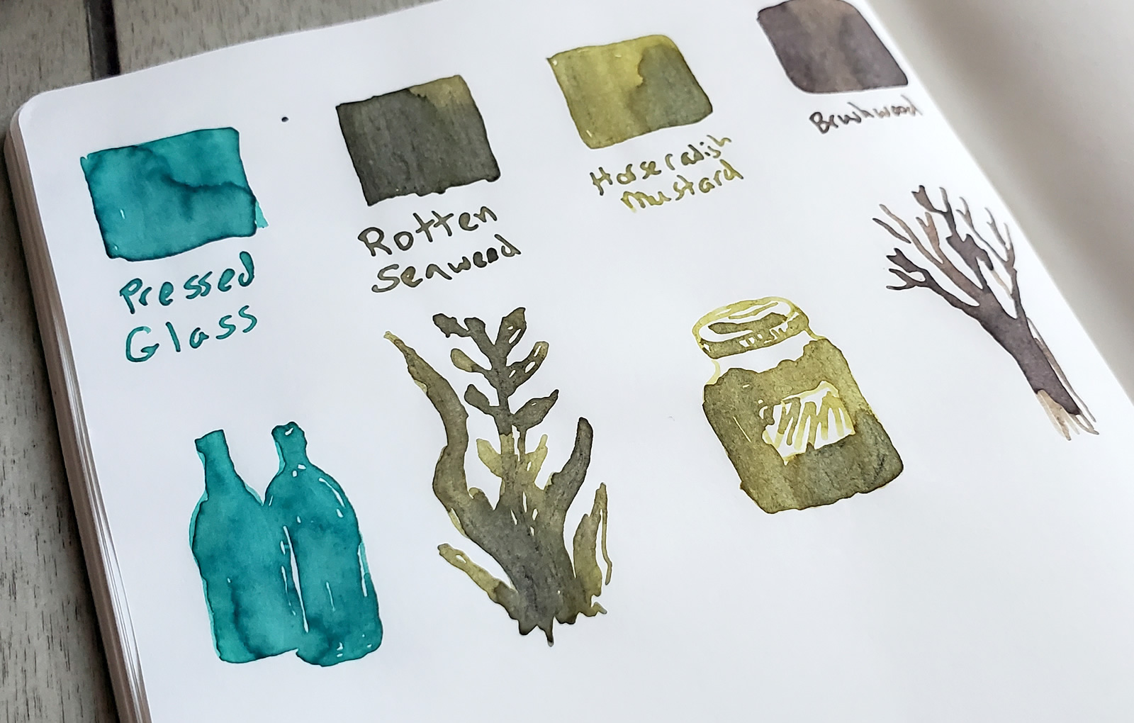 Journal page with ink swatches of four Birmingham Pen Co. inks, including little sketches related to each ink name. The inks are Pressed Glass, a rich teal, Rotten Seaweed, dark yellow-green, Horseradish Mustard, brighter yellow-green, and Brushwood, a reddish gray-brown.