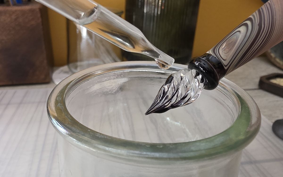 A glass dropper dripping water onto the glass nib diluting the ink on the nib.