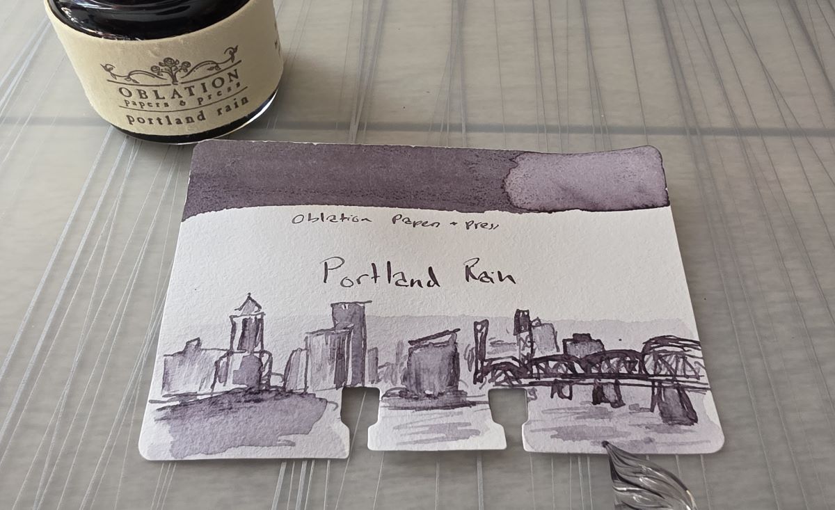An outline of the Portland skyline and bridge with water in the foreground that has been softened and shaded in with diluted ink.