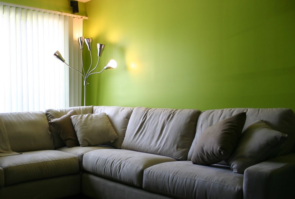 A living room wall painted bright chartreuse green with a neutral color sectional couch, lamp, and windows.