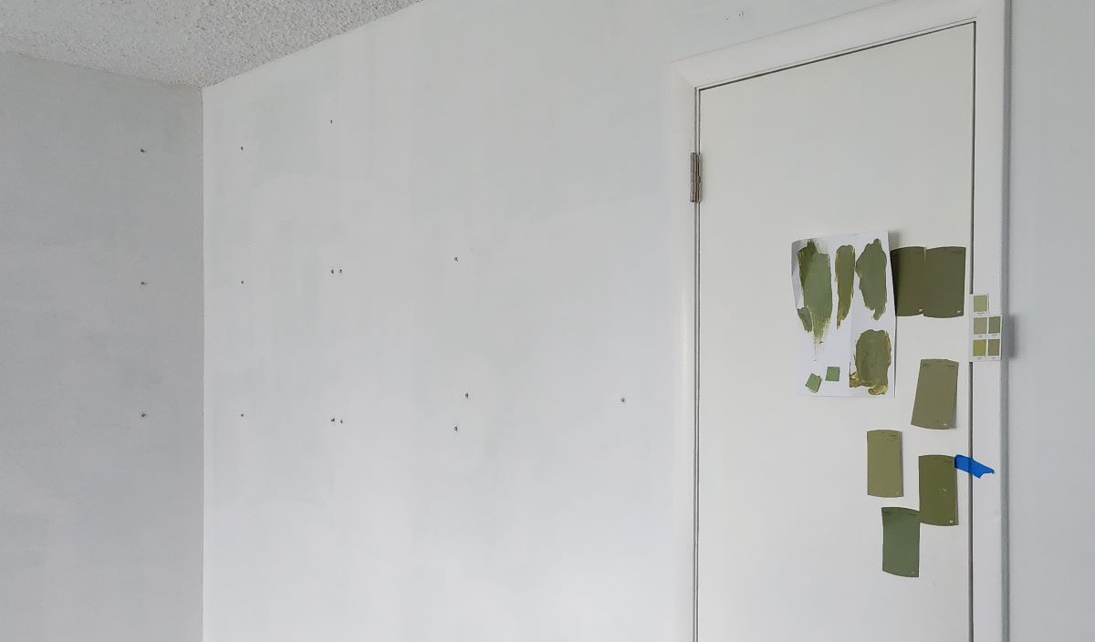 The corner of a room and closet door all painted bright white, with a variety of green paint swatches taped to the door.