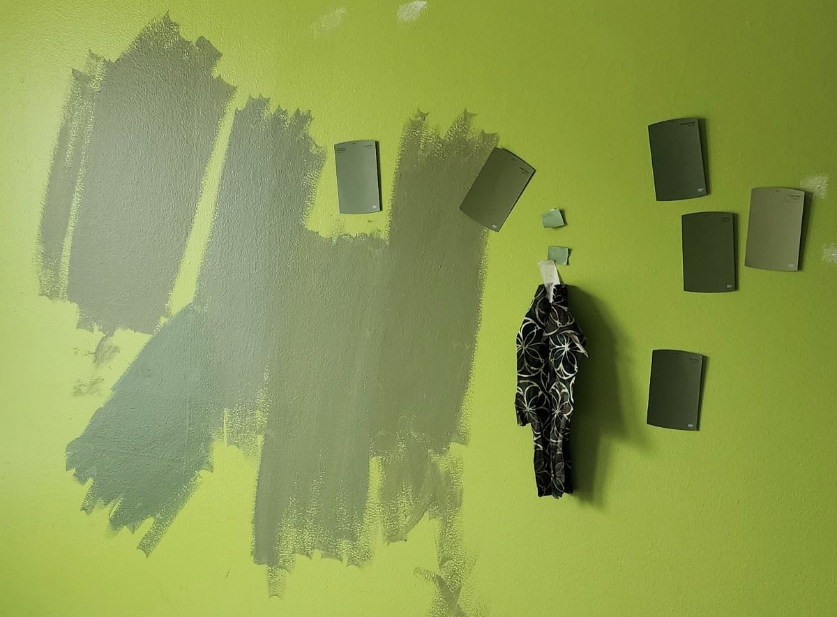 A chartreuse green wall with a variety of green paint chips and a scrap of fabric taped to the wall and paint samples painted on the wall