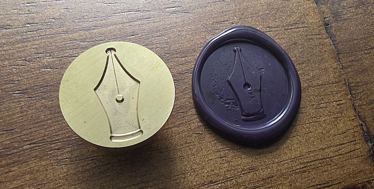 A metal wax seal with simple pen nib design and a round dark purple wax seal with that design pressed into the wax.