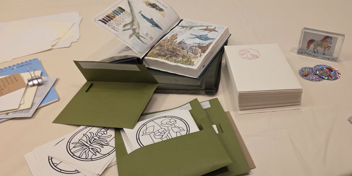 Loose fountain pen papers for testing, Dominant Industry Ink Archiving book open to painted page of sea creatures, papers with things to color being sorted into envelopes, stack of envelopes and holographic stickers.