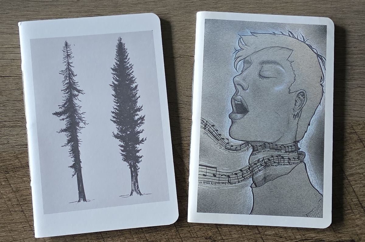 Two small staple bound notebooks with art on the covers, one of two tall, skinny evergreen trees and the other with a person singing with mouth open, eyes closed, and a staff with music notes wrapped around their throat.