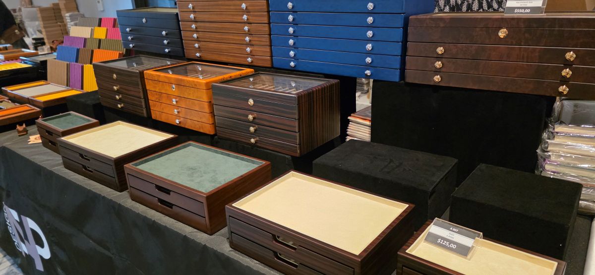 A table at a pen show with several large, wooden pen storage boxes with multiple drawers in various shades.