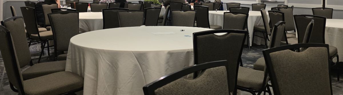 Several large round tables surrounded by chairs in a breakout room at a hotel.