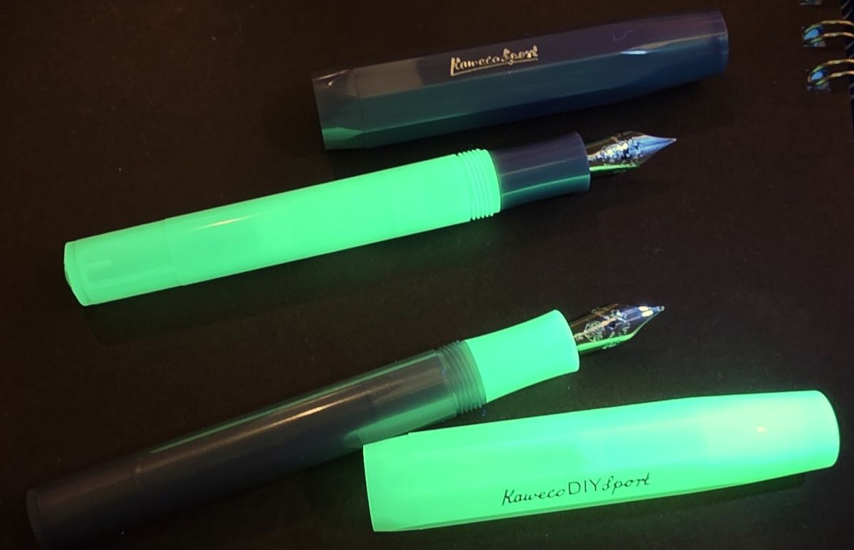 Uncapped DIY Glow Green and Lunar Green Shadow Kaweco sport pens with swapped sections under UV light so the glow-in-the-dark material is glowing bright green. 