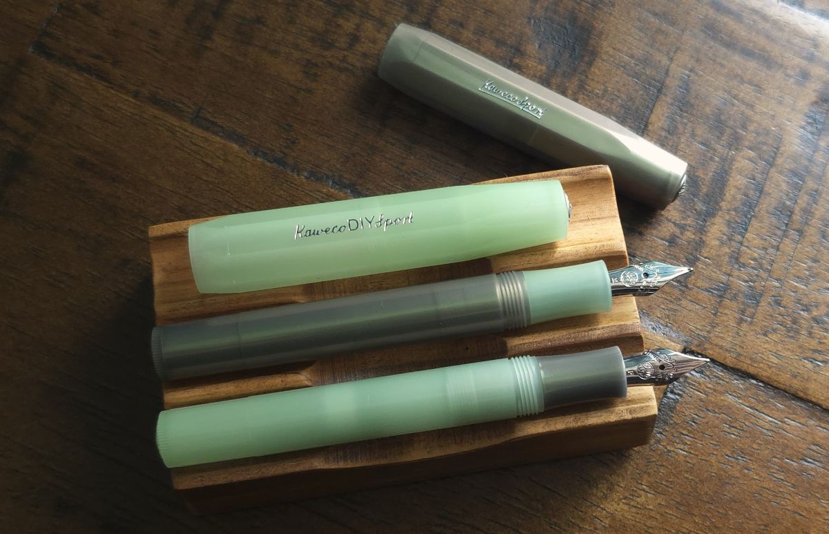 Uncapped DIY Glow Green and Lunar Green Shadow Kaweco sport pens with swapped sections on a pen rest in daylight.