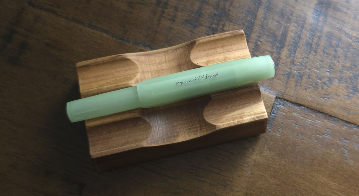 An assembled Kaweco DIY Sport Glow Green fountain pen on a wood pen rest.