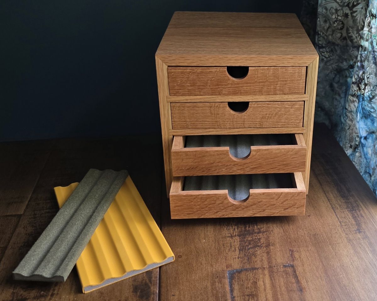A compact wooden box with four drawers with gray liners to hold six pens each, a 4 slot yellow leather pen tray and a 2 slot dark green pen tray.