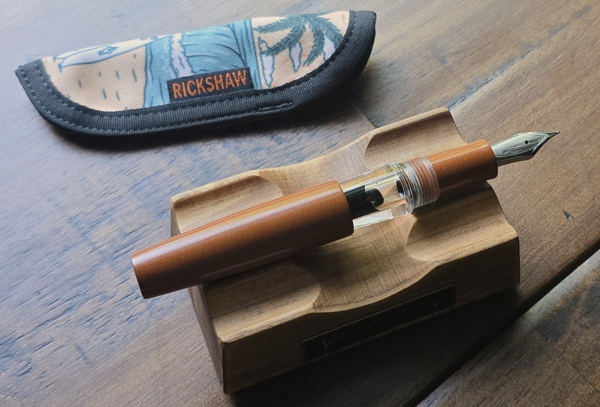 Uncapped LVED fountain pen with orange brown ebonite cap and section and clear body, with surfboard design on nib.