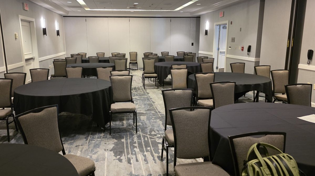 The empty Vanness Pen Lounge with eight round conference tables with black table cloths surrounded by chairs.