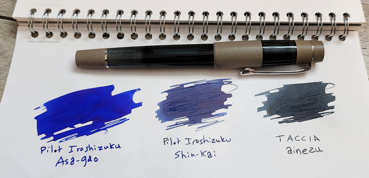 Comparison swatches of the bright blue of Pilot Iroshizuku Asa-Gao, the dusty blue black with red sheen of Pilot Iroshizuku Shin-Kai, and the green-tinged dark blue gray of Taccia Ainezu, next to the Opus 88 Koloro pen in dark teal acrylic and gray brown ebonite.