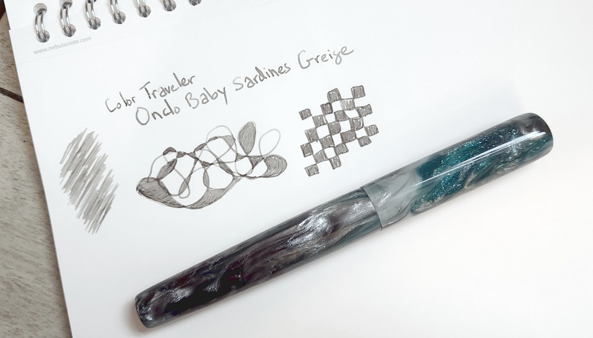 A writing sample of the warm medium gray Color Traveler Ondo Baby Sardines Greige ink, next to a London Pen Co. pen in Argent Emerald material with swirls of sparkly bluegreen, silver, and gray.