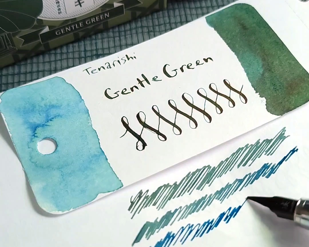 A close-up view of a Col-o-ring card for Teranishi Gentle Green and lines being drawn that show how the fresh ink looks very blue and the dried ink looks green with a slight red sheen.