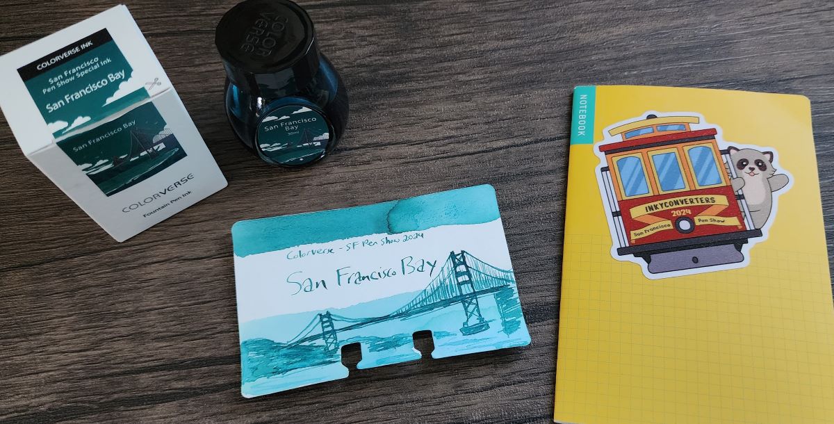 Bottle and Col-o-dex card with sketch of the Golden Gate bridge for Colorverse San Francisco Bay, a shading teal ink. Small yellow pocket notebook with sticker of trolly and racoon from Inky Converters for the 2024 San Francisco Pen Show.