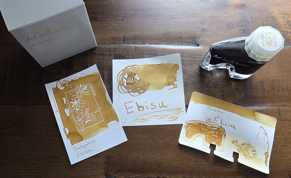 Three swatch cards for the warm golden yellow Bungubox Ebisu ink and the signature 'boot' shaped glass bottle.