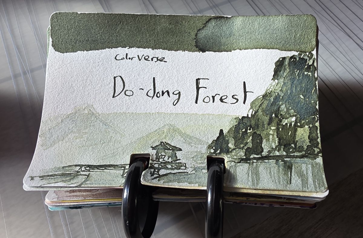 A Col-o-dex ink swatch card for Colorverse Do-dong Forest, a medium gray green with yellow undertones, with a sketch of a forested island and dock on the water.