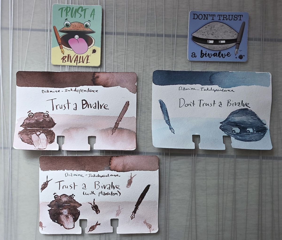 Two stickers with cartoon sketches for Trust a Bivalve and Don't Trust a Bivalve with three Col-o-dex swatch cards with similar sketches for the corresponding Diamine inks, the warm taupe Trust a Bivalve and medium gray blue Don't Trust a Bivalve.