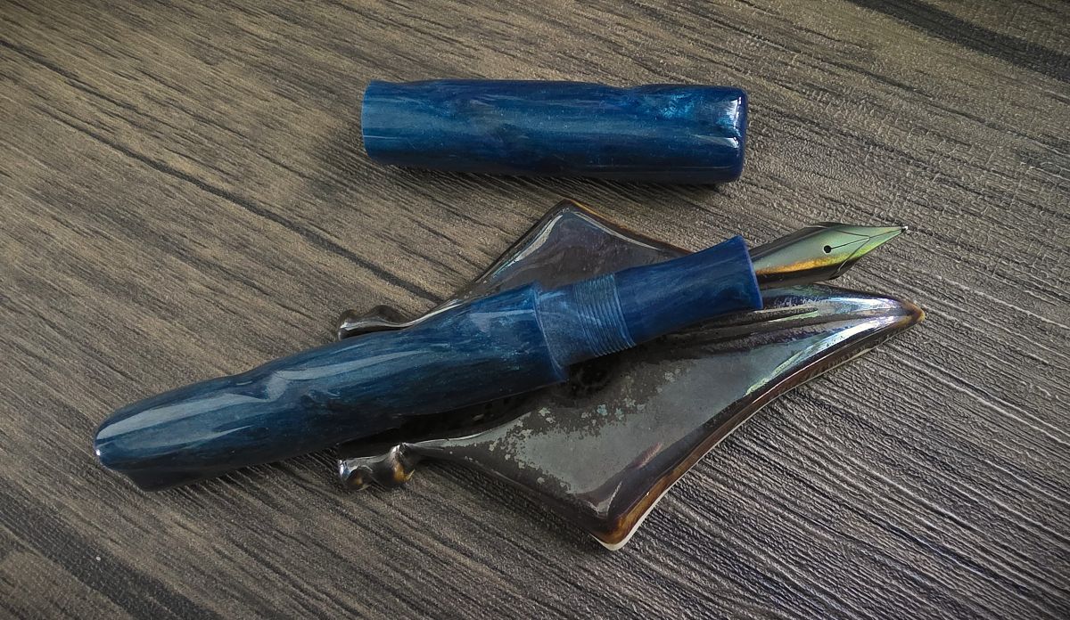 A hand-carved fountain pen in blue resin with a carved spiral along the whole length of the pen, cap off with an iridescent fountain pen nib.
