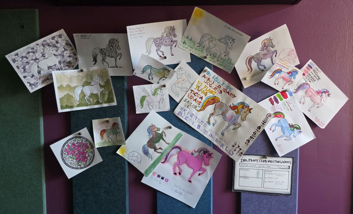 Colorful felt panels on a dark magenta wall with several sheets of paper held up by magnet pins with ink ponies painted in a wide variety of colors and styles created by several different people.