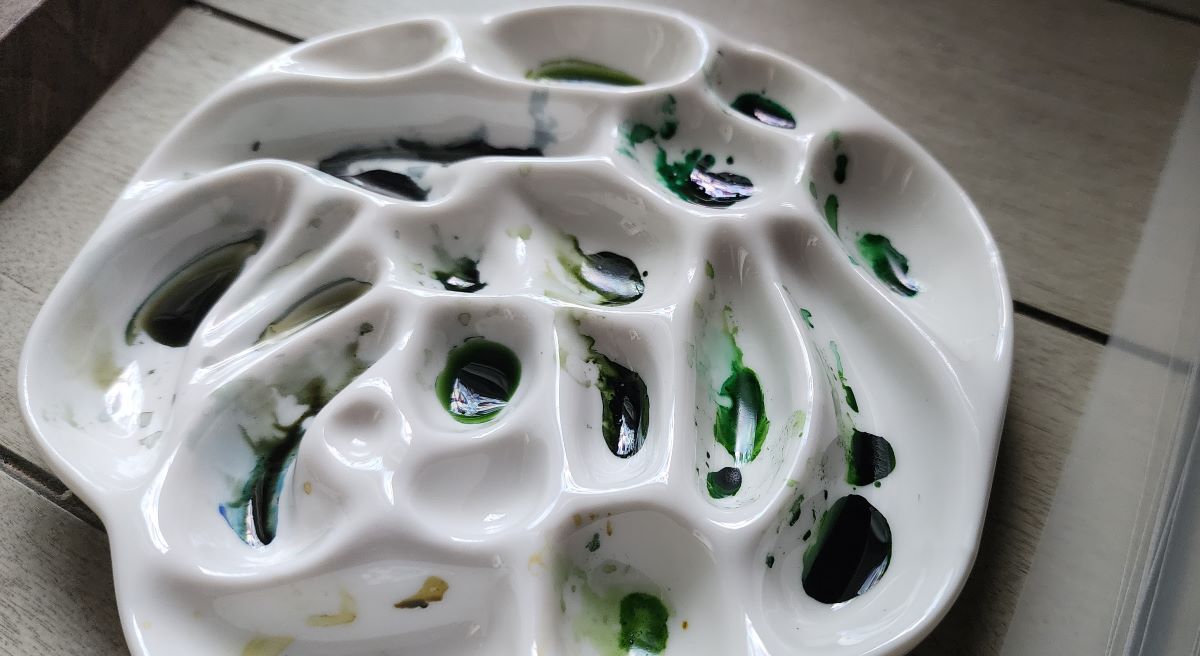 Asymmetrical round ceramic paint palette with the residue of several green inks in the bottom of the wells.