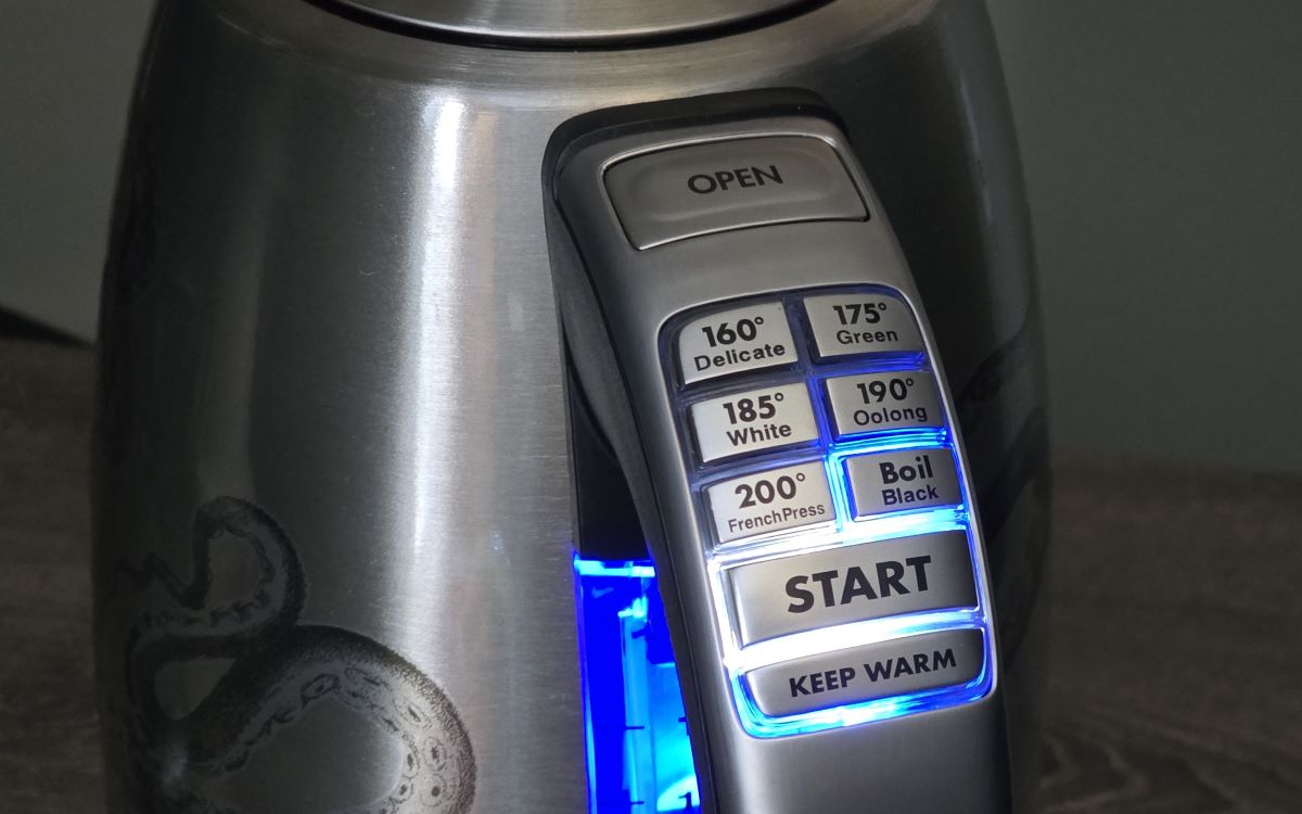 Close up of handle of large electric kettle with buttons to heat water to 160°F for Delicate, 175°F for Green, 185°F for White, 190°F for Oolong, 200°F for FrenchPress, and Boil for Black, plus buttons to Start and keep warm, and the buttons and water level on kettle are lit up blue.