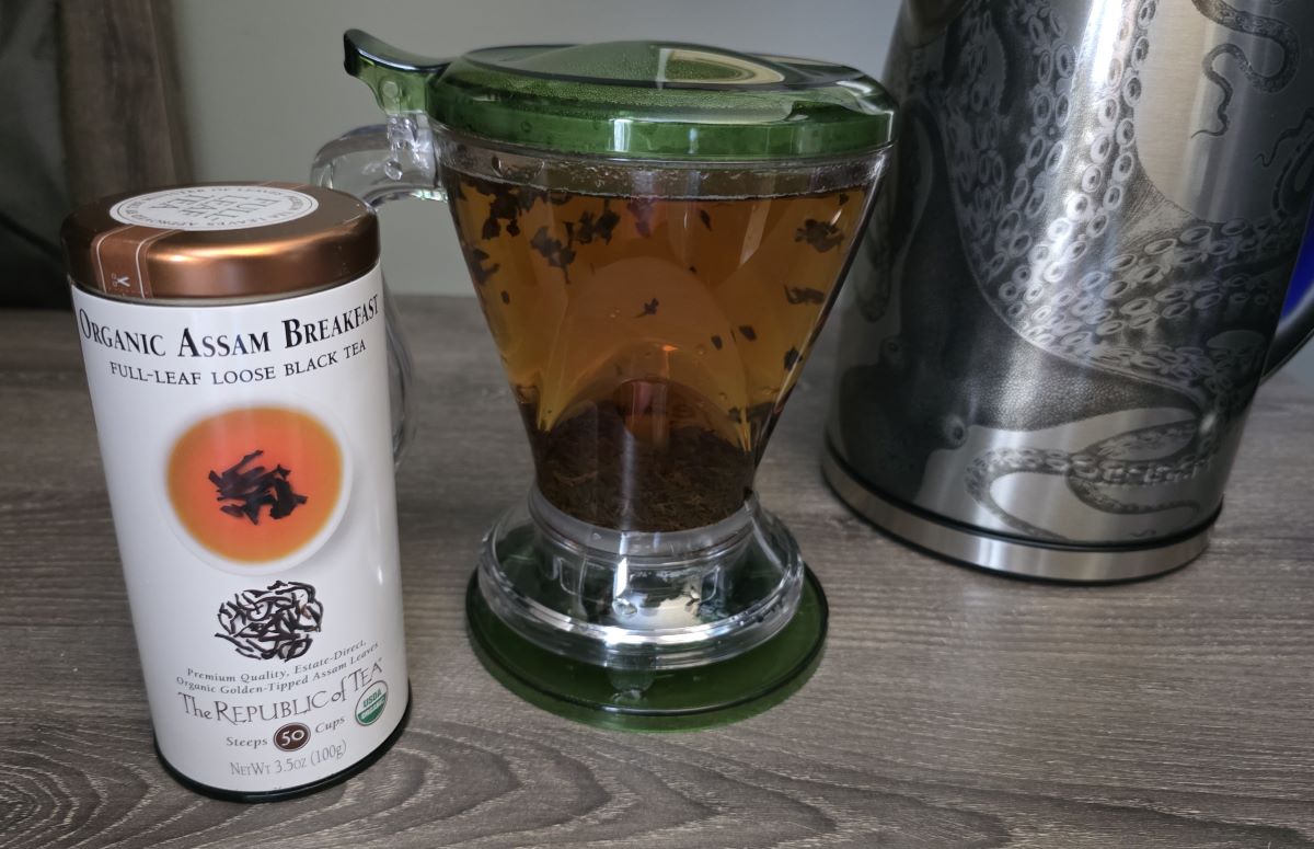 The Teaze tea infuser filled with water and steeping Organic Assam Breakfast loose-leaf black tea, next to the tin of tea and electric tea kettle.