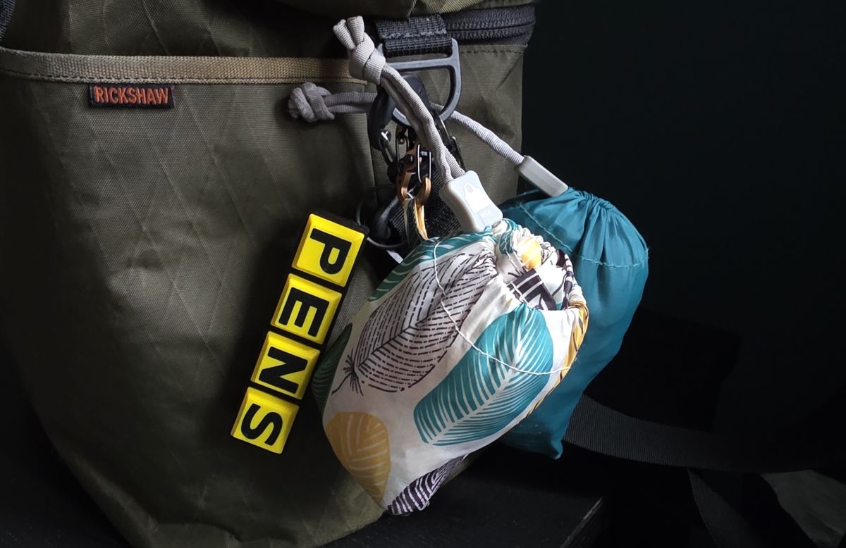 Side of a large green bag with two reusable bags tucked into pouches and clipped to a ring of the shoulder strap.