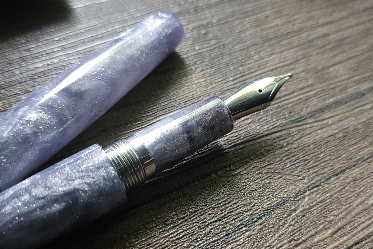 Closeup of section, nib, and cap of a light dusty purple fountain pen.