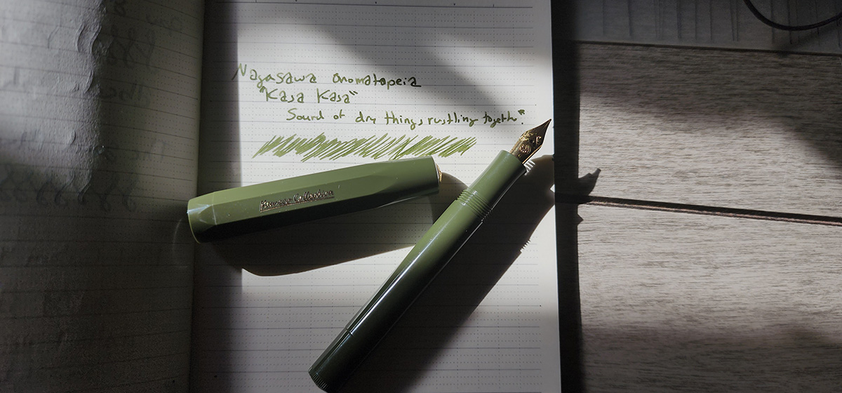 A dark olive plastic pocket fountain pen with a gold tone nib shining in a beam of sunlight.