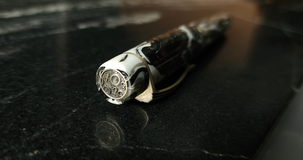 Close up view of a silver moon insert in the top of the cap of a fountain pen with a swirled white and black pen.