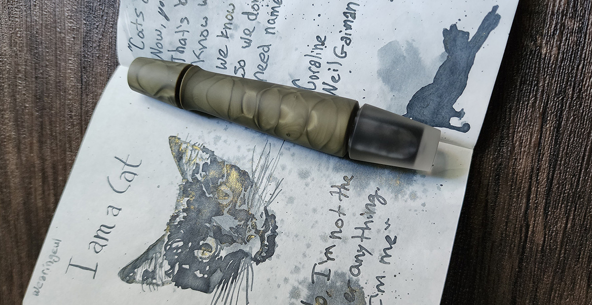 A short, uniquely-shaped fountain pen with a small plug cap, flared section and tapered body in a matte olive green chatoyant material and short frosted clear section at the base.