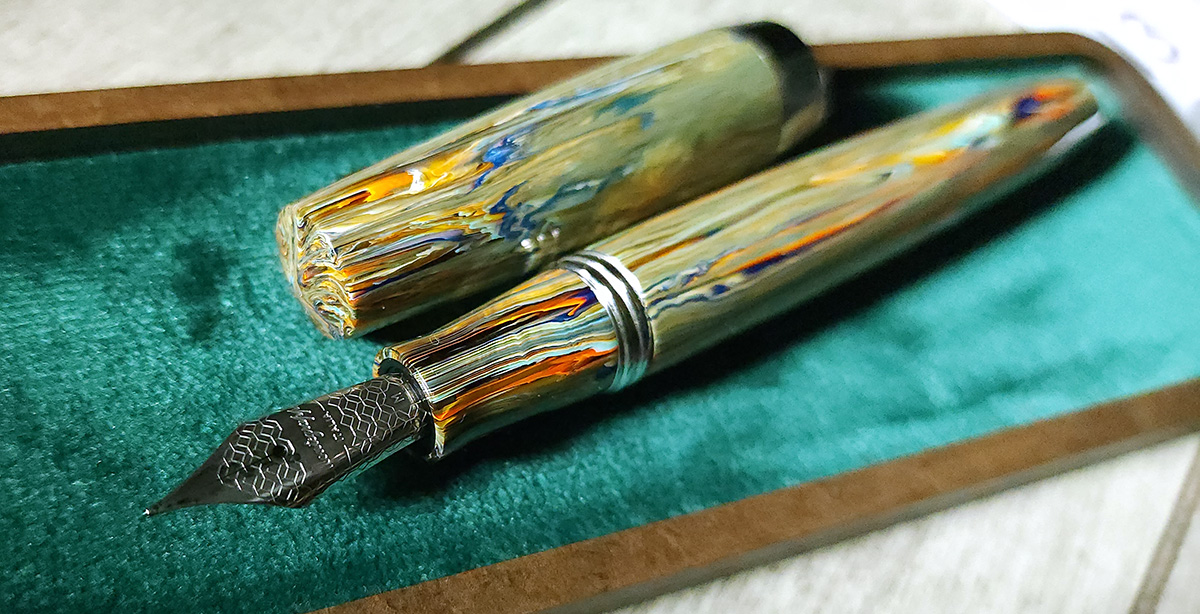 A closeup of the nib on a Montegrappa Elmo 02 pen in the Nirvana colorway which has vertical streaks of gray green, blue, orange, white and clear.