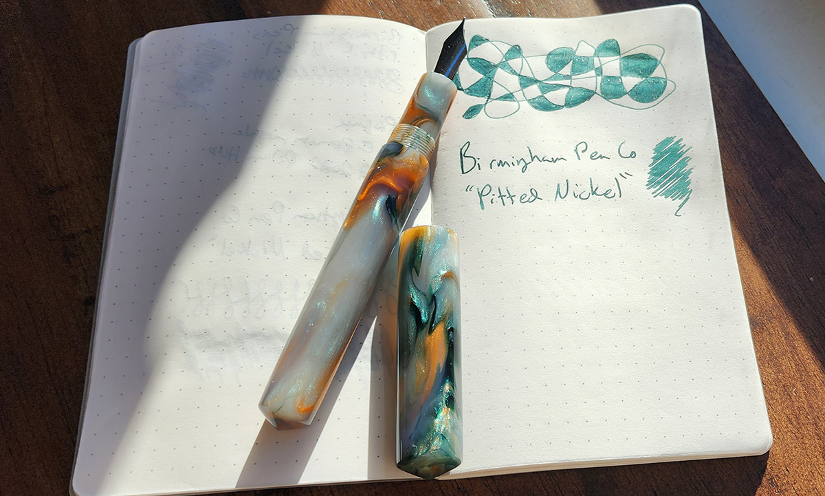 A turned resin fountain pen in a pearl white with swirls of orange and dark blue green.