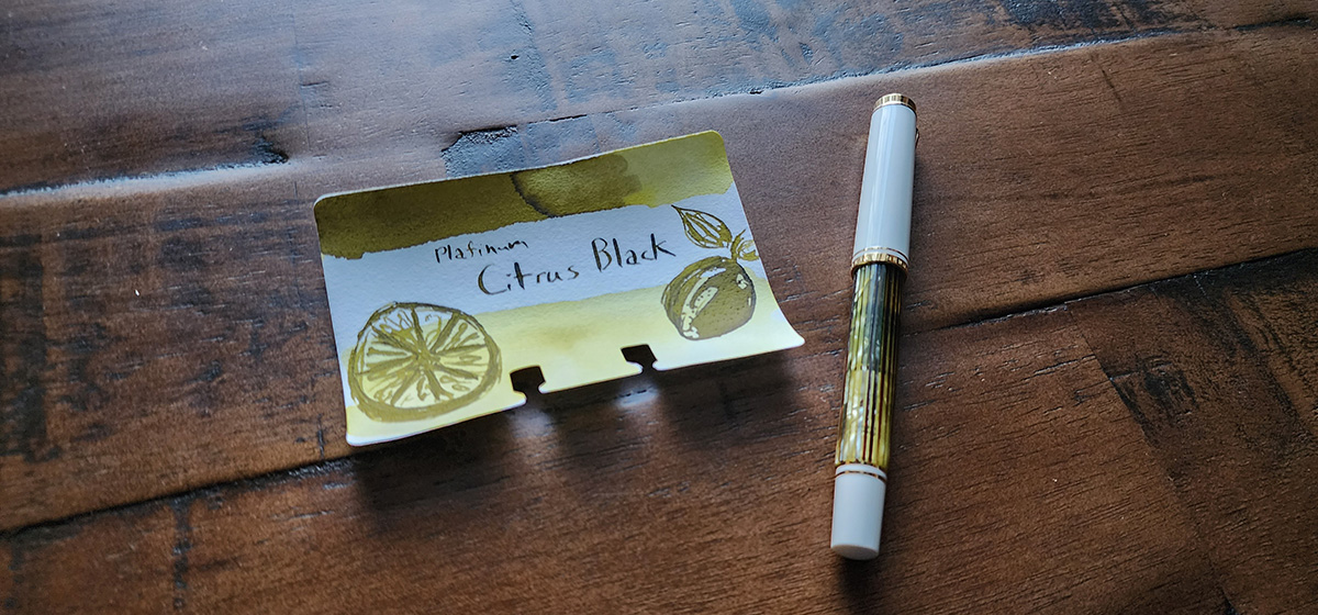 A Pelikan Souverän M400 in Tortoiseshell White with a translucent yellow-green striped body, white cap and end, gold trim, next to an ink swatch and sketch of lemons for Platinum Citrus Black ink.