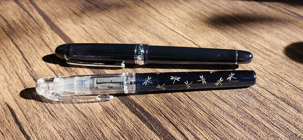 A slightly translucent black Platinum 3776 fountain pen and a Preppy Wa fountain pen with a clear cap with translucent dark blue body with silver and gold dragonfly design.