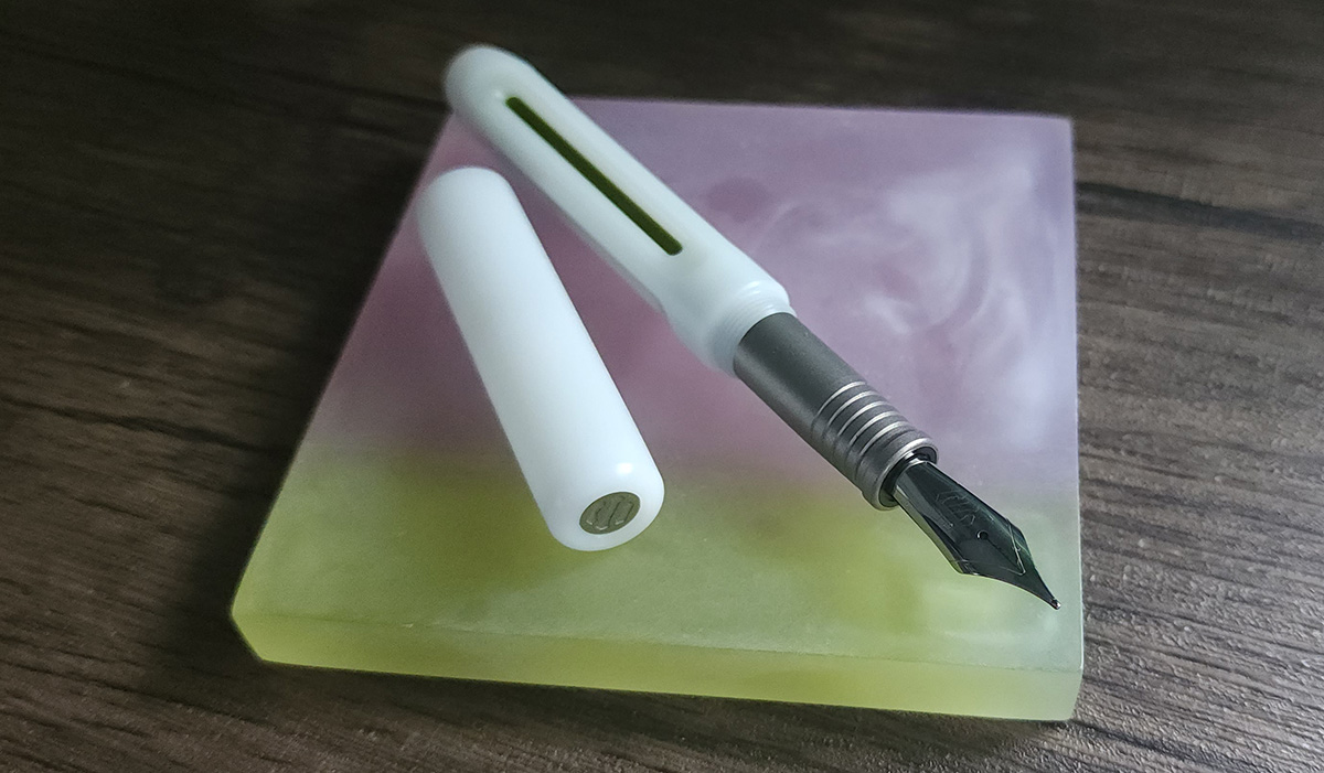 A bright white fountain pen with gray section and vertical cutouts in the body showing metallic green.