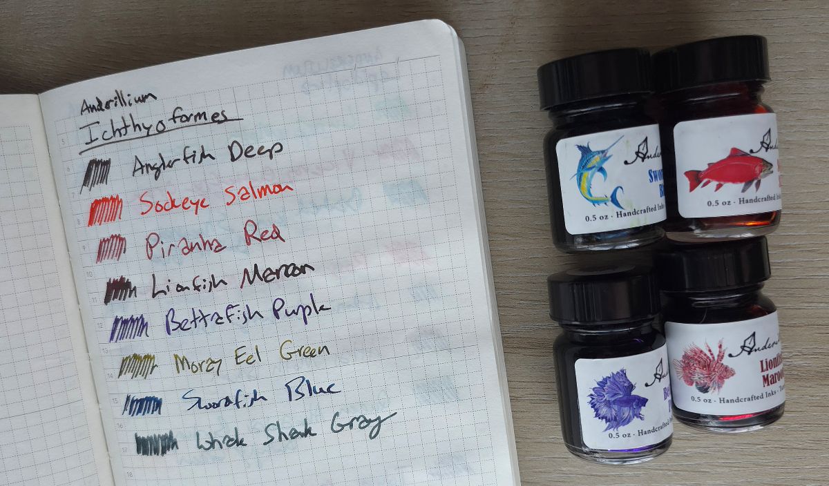 A notebook with writing tests for all eight Anderillium Icthyformes inks and small bottles of Swordfish blue, Sockeye Salmon, Betta Fish Purple, and Lionfish Maroon.