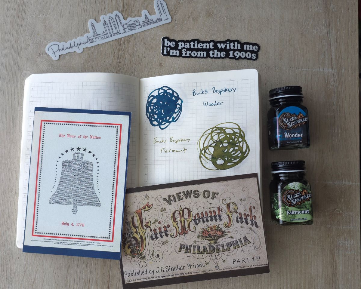 A notebook with swatches of Bucks Bespokery inks Wooder and Fairmont along with postcards with vintage designs for the Liberty Bell and Fair Mount Park and vinyl stickers of the Philadelphia skyline and 'Be patient with me I'm from the 1900s' text.